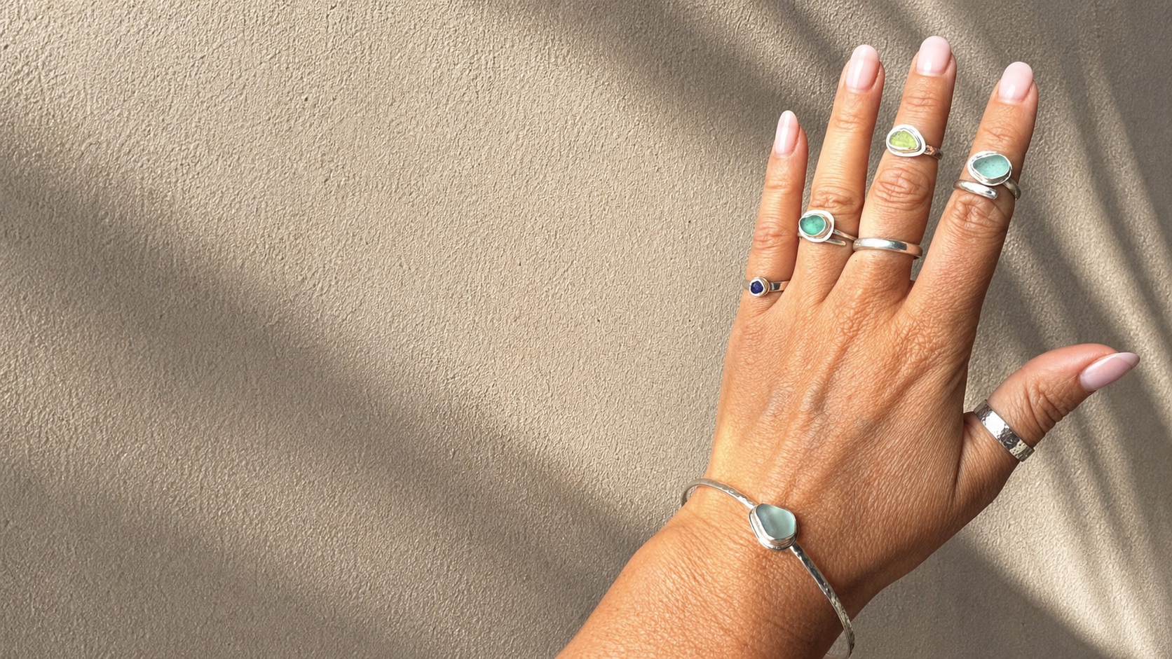 Hand wearing Ellis Made sea-glass rings and a silver bracelet